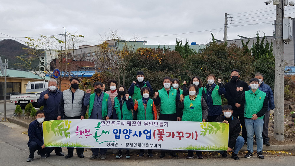 청계면 행복홀씨 입양사업(꽃가꾸기) 청계면 청계면 새마을 부녀회 현수막뒤에서 사람들이 단체사진을 찍고있다. 