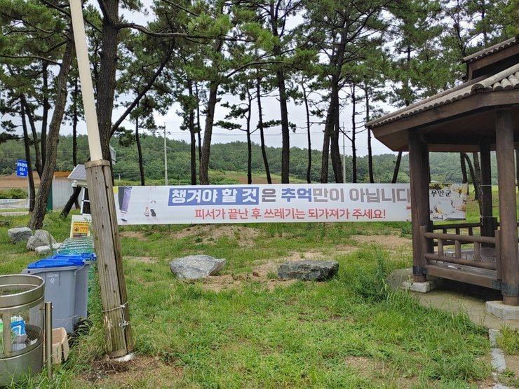 해변 입구에 '챙겨야 할 것은 추억만이 아닙니다. 피서가 끝난 후 쓰레기느느 되가져가 주세요!'라는 문구의 현수막이 설치되어 있다.